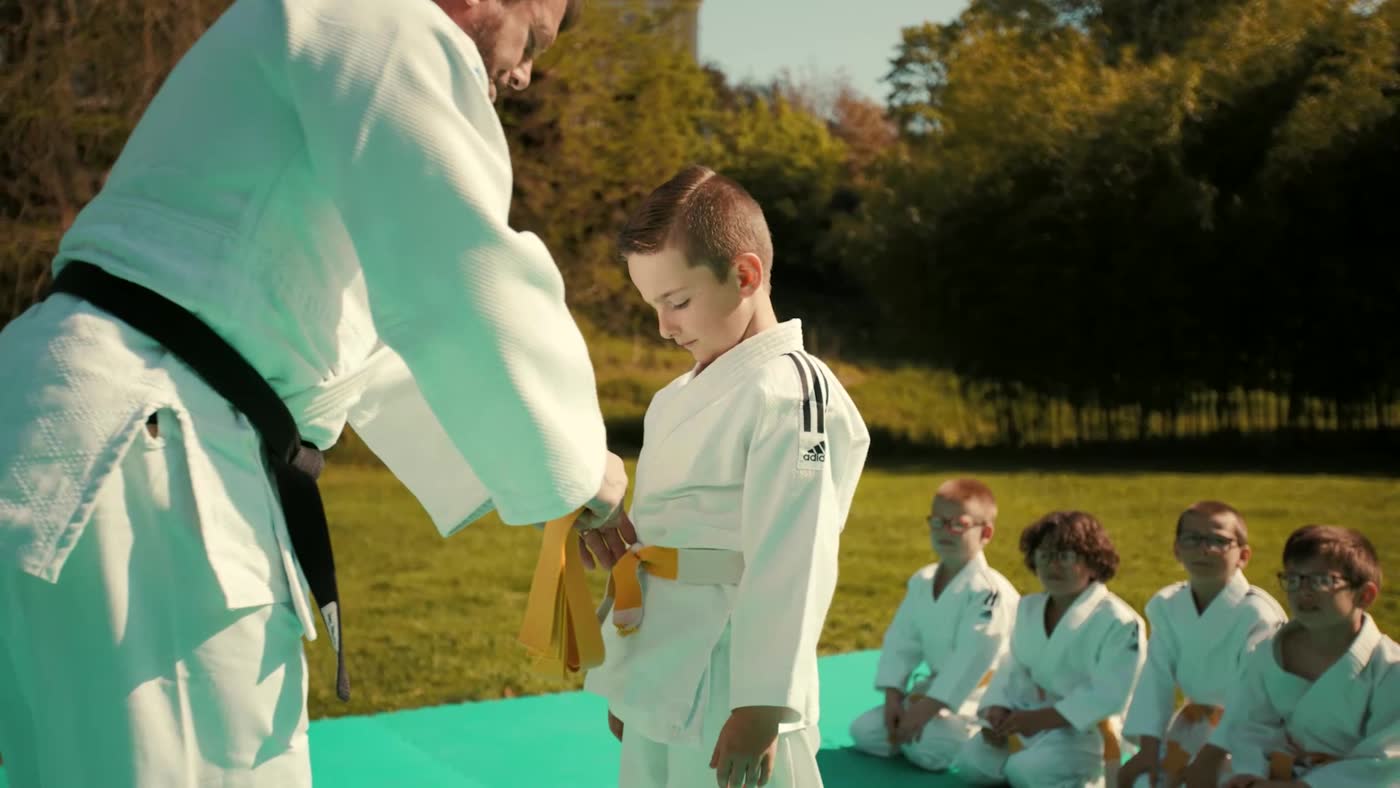 Tableau 4 — Passage de ceinture. « Un élève reçoit une ceinture jaune de la part de son professeur. La première étape de la vie du judoka. »